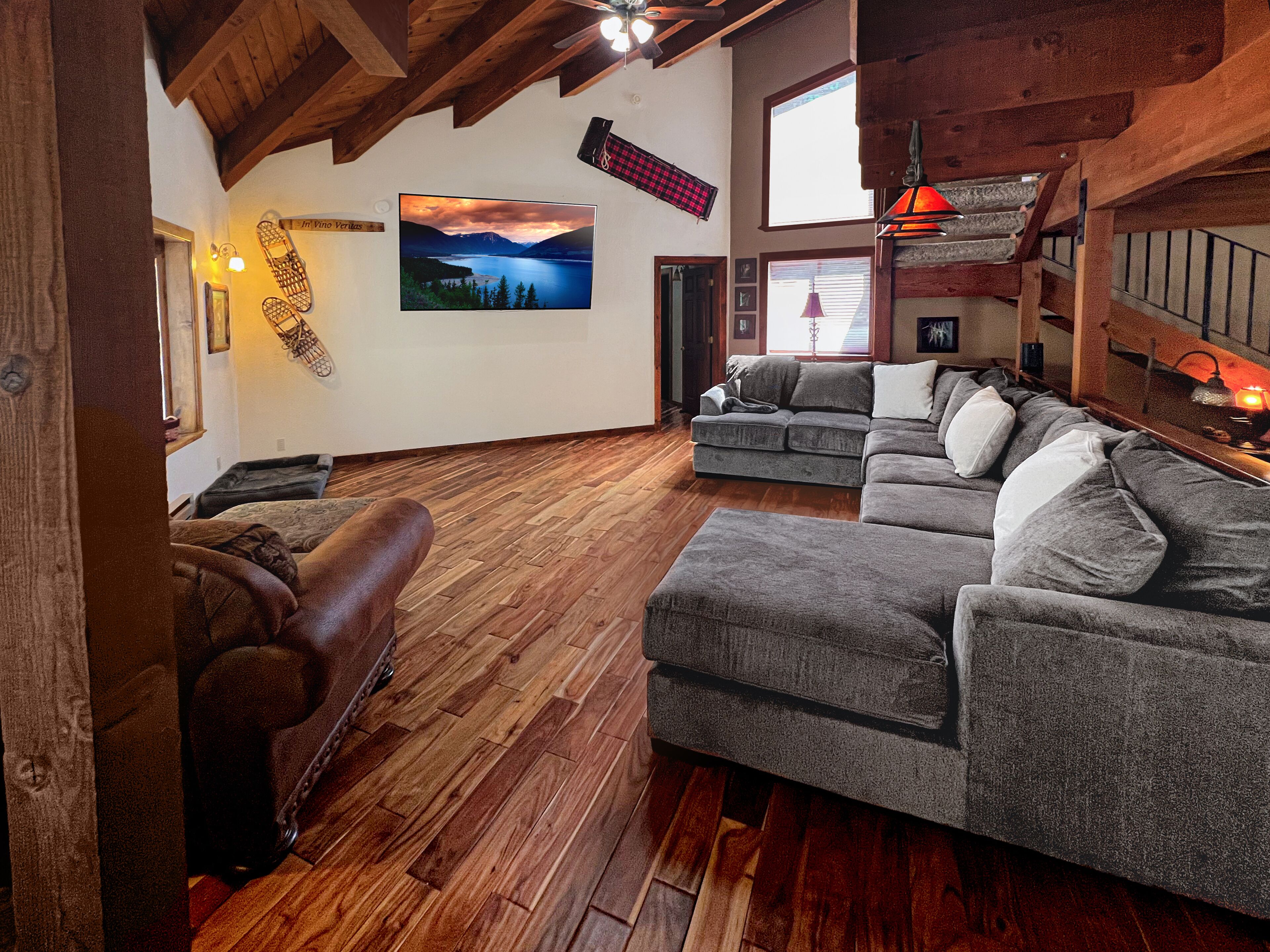 A spacious living area with wooden flooring, a large gray sofa set, a brown leather couch, and a fireplace.