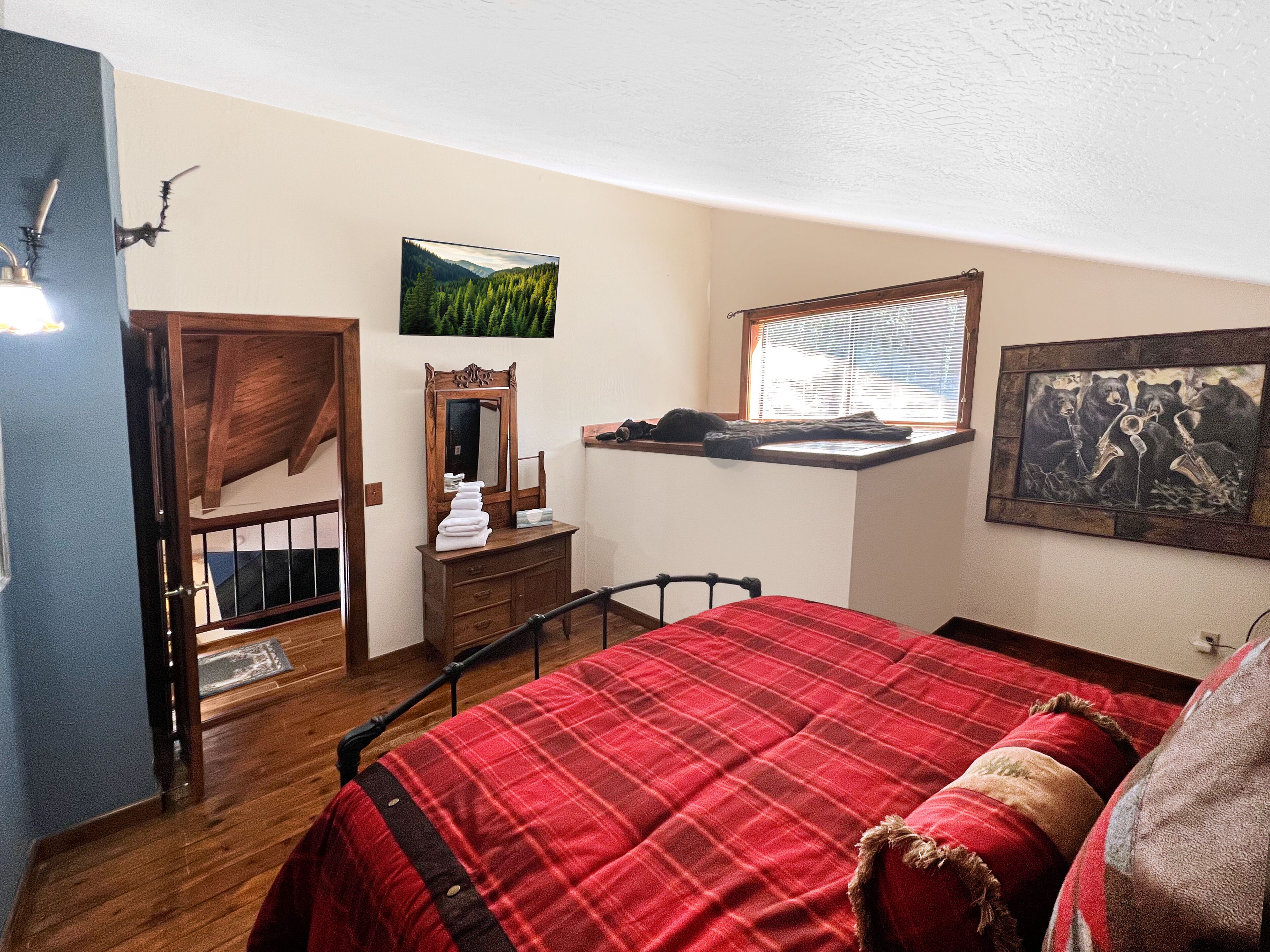A bedroom with a bed, dresser, mirror, window, and artwork.