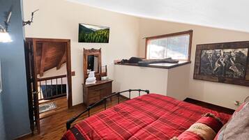 A bedroom with a bed, dresser, mirror, window, and artwork.