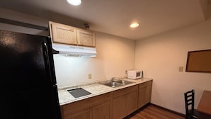 A compact kitchen with wooden cabinets, a black refrigerator, a microwave, and a sink. - Relax Inn & Suites (Mattoon)