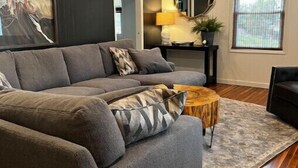 A modern living room with a grey sofa, a round wooden coffee table, and a large mirror. - Big Stone Lake, SD-Bayview area Lake Cabin (Big Stone City)