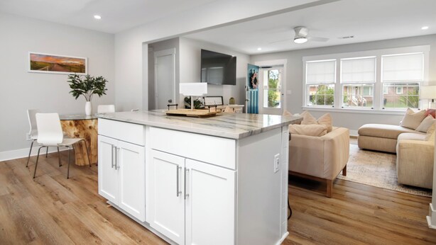 A modern kitchen with white cabinets, a marble countertop, and a dining area with a wooden table and chairs.