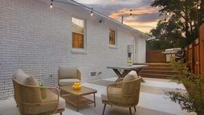 A patio with wicker chairs and a table, a white brick house, and a wooden fence.