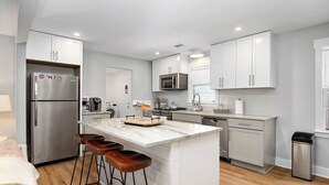 A modern kitchen with white cabinetry, a stainless steel refrigerator, a microwave, and a central island with stools.