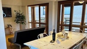Ein Essbereich mit einem weißen Tisch, weißen Stühlen und einem schwarzen Sofa. Eine Pflanze und ein kleiner Tisch mit einer Flasche und einer Kerze sind ebenfalls vorhanden.