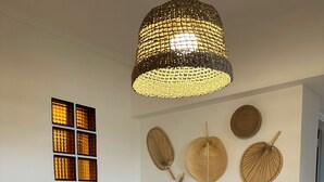 Ein Zimmer mit einer gewebten Pendelleuchte, einem Wandventilator und einem Tisch mit Lampe und Dekoration.