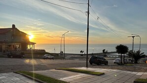 Eine Küstenstraße mit einem Gebäude links, Autos am Straßenrand und einem Sonnenuntergang im Hintergrund.
