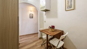 A small room with a wooden table, white chairs, a basket of flowers, a framed picture on the wall, and a white ceiling vent. - Artist's Refuge in Florence by Mmega (Firenze)