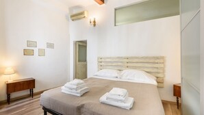 A bedroom with a bed, two bedside tables, a wall-mounted air conditioner, and a door. - Artist's Refuge in Florence by Mmega (Firenze)