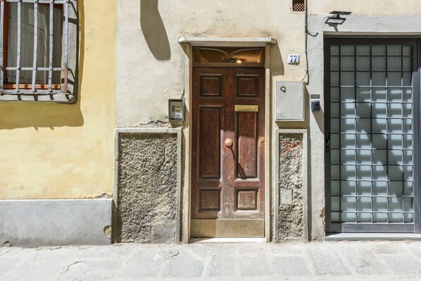 Une porte en bois avec une poignée en laiton, une boîte aux lettres et une plaque numérotée « 77 » sur la façade d’un immeuble.