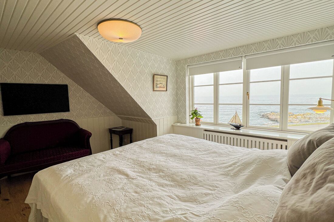 A bedroom with a large bed, a red sofa, a window with a view of the sea, and a decorative ceiling light.