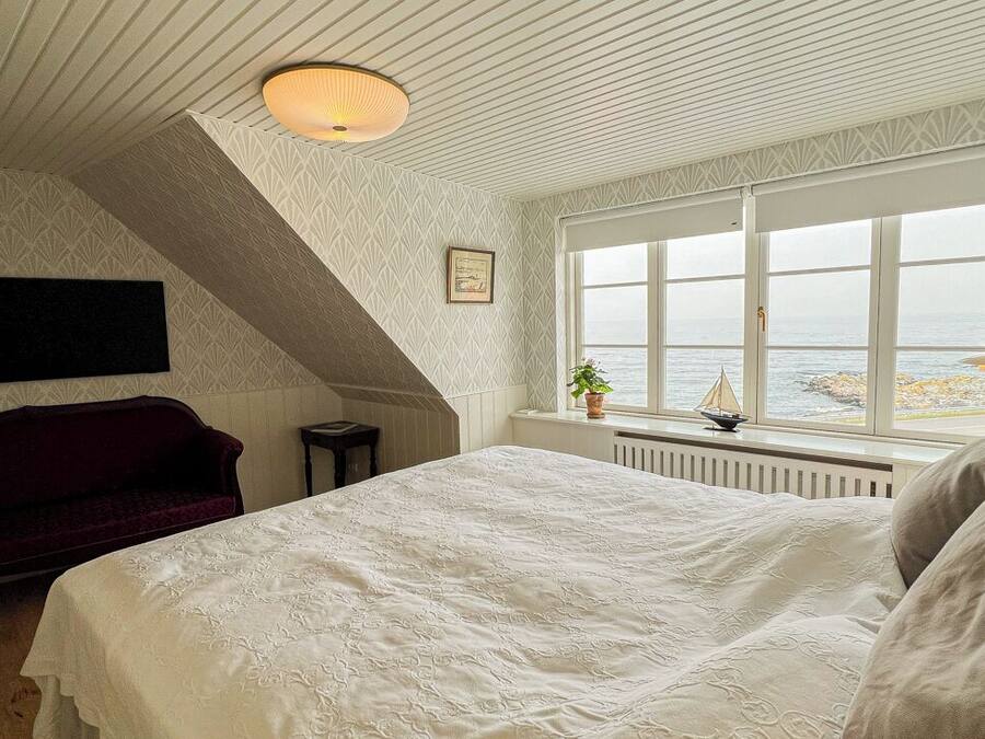 A bedroom with a large bed, a red sofa, a window with a view of the sea, and a decorative ceiling light.