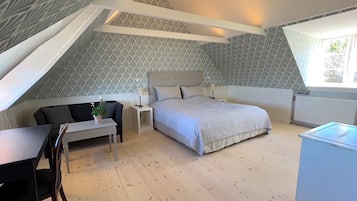 Un dormitorio con techo inclinado, una cama con cabecera, un escritorio con silla, una mesita con una planta y un radiador.