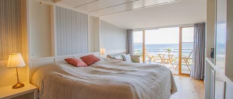 Ein geräumiges Schlafzimmer mit einem großen Bett, einem Nachttisch mit Lampe und Meerblick vom Balkon.