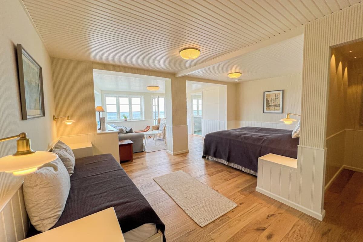A spacious bedroom with a large bed, a sitting area with a sofa and a small table, and a view of the sea through large windows.