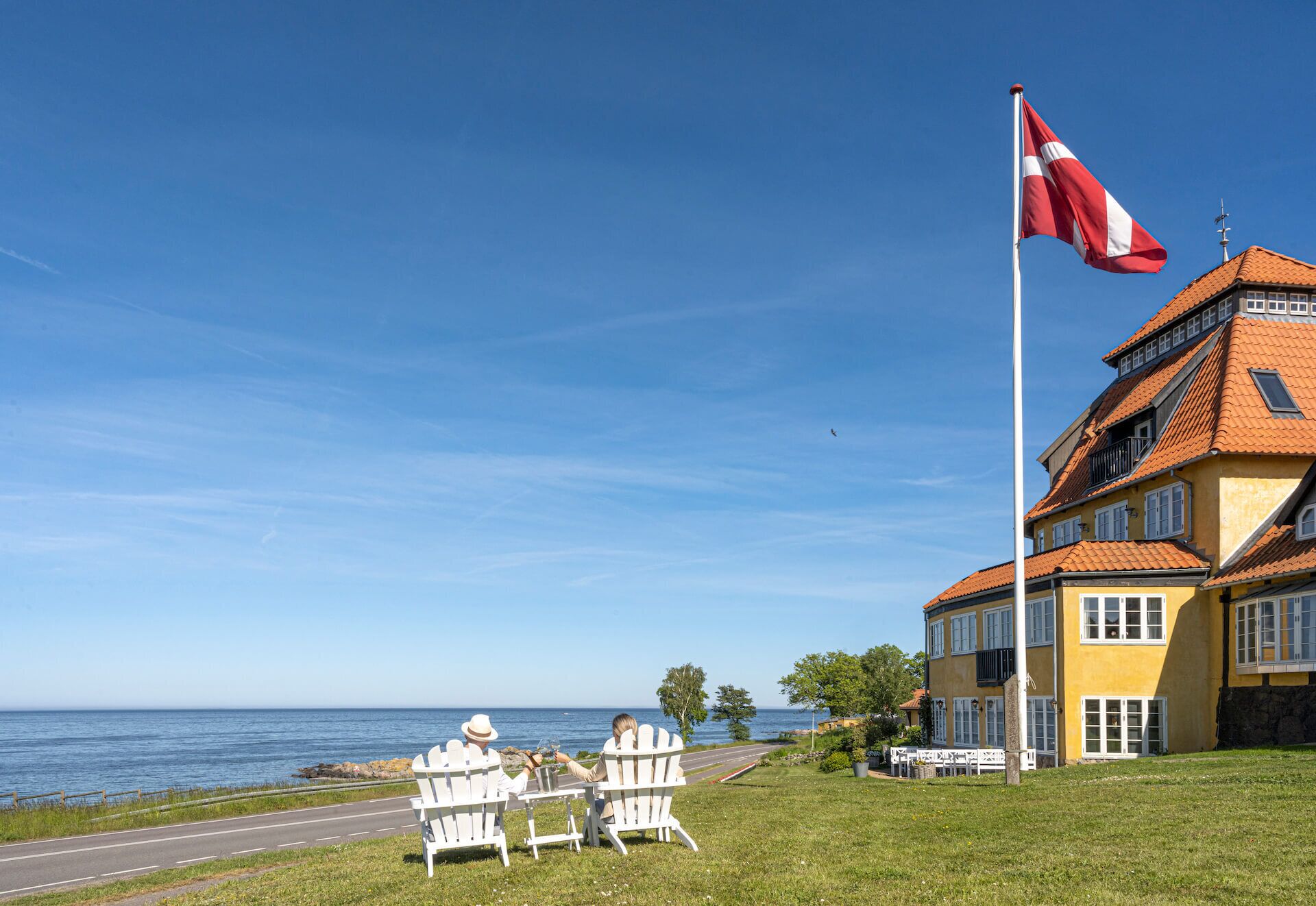 En byggnad vid kusten, med en flagga, en väg och utsikt över havet.