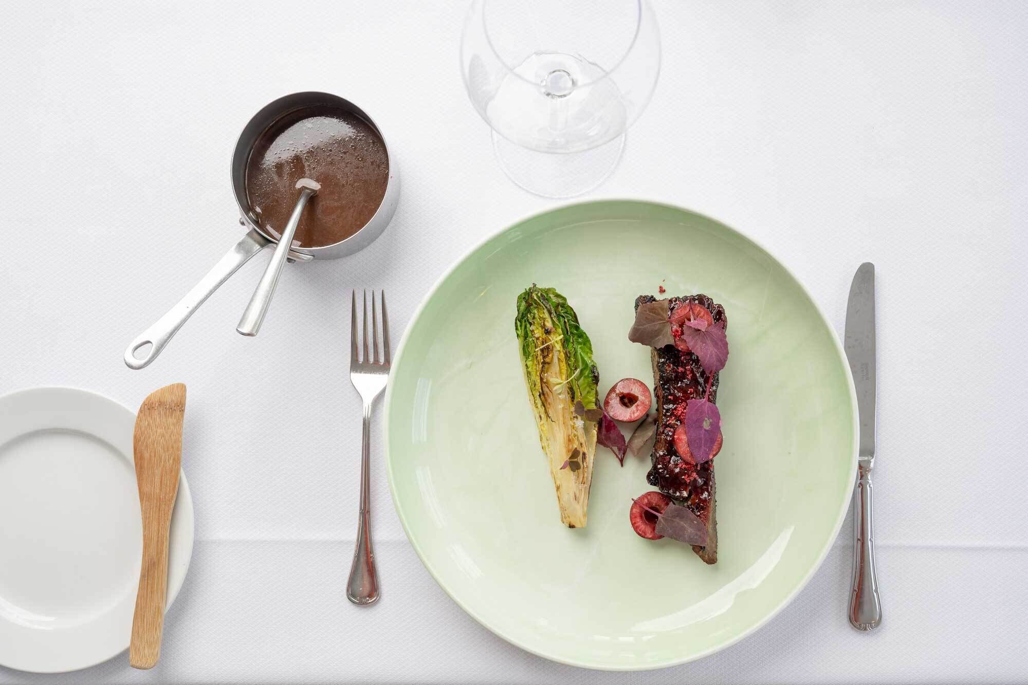 A plate with a green salad, a glass of wine, and a small bowl of salt on a white table.