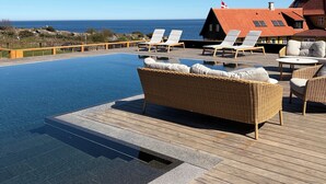 A infinity pool with lounge chairs and a wooden deck overlooking the ocean. - Stammershalle Badehotel & Spa (Gudhjem)