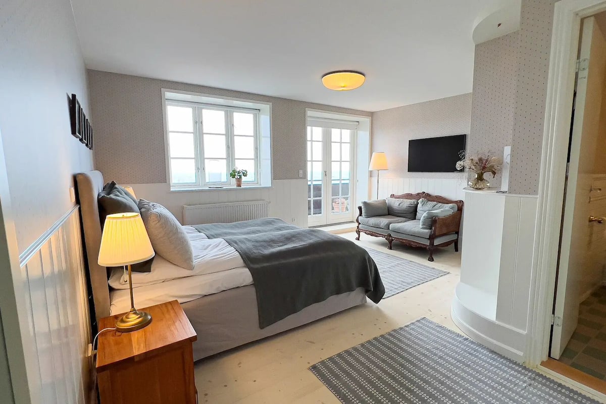 A bedroom with a bed, bedside tables, a sofa, a TV, and a window.