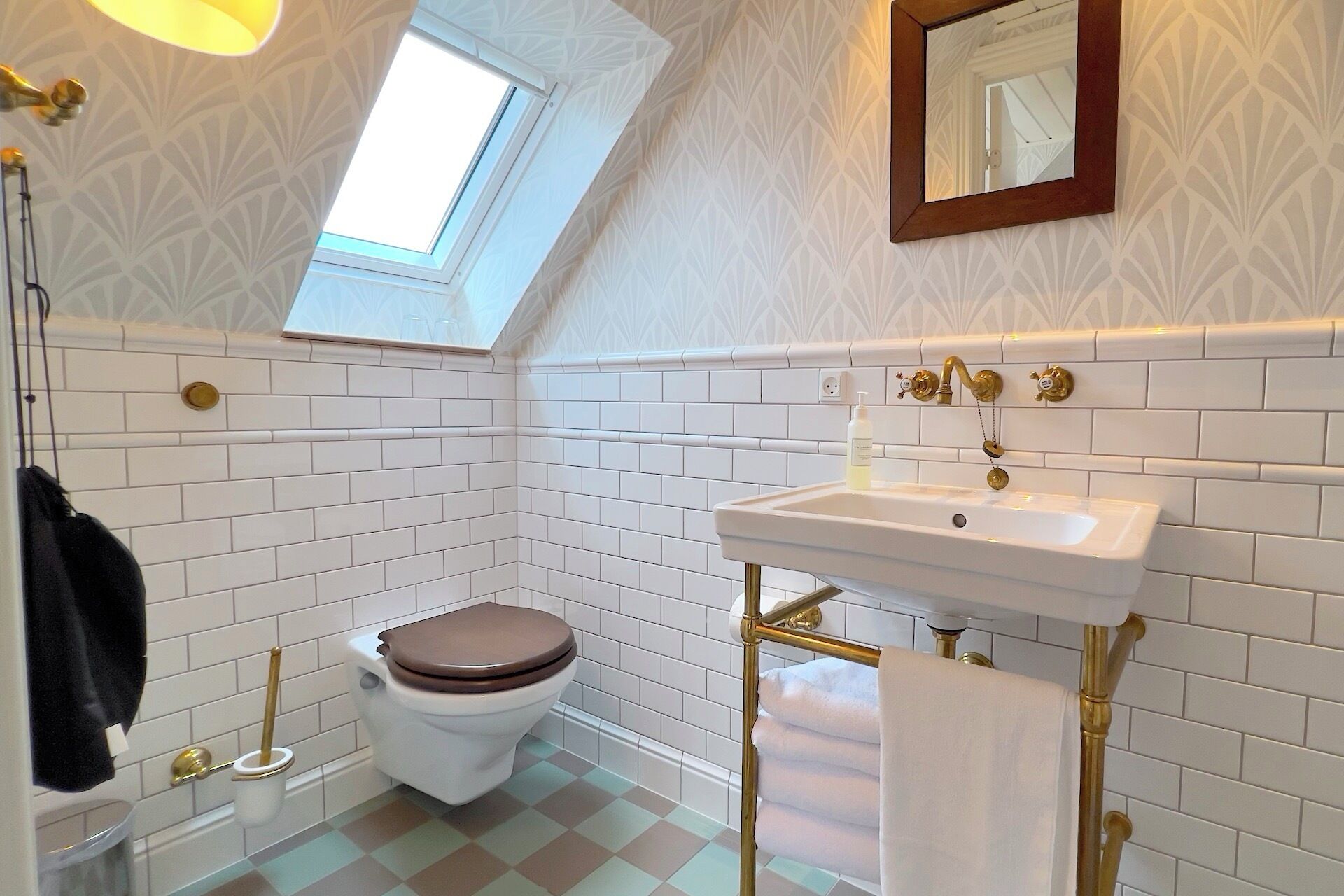 A bathroom with white subway tiles, a white toilet, a gold sink, and a towel rack.