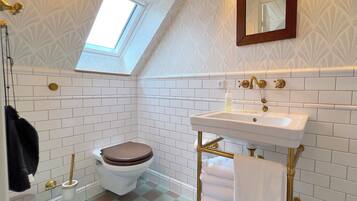 A bathroom with white subway tiles, a white toilet, a gold sink, and a towel rack.