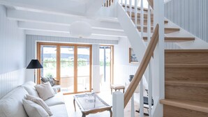 A spacious living room with a white staircase, a sofa set, and a dining area. - Stammershalle Badehotel & Spa (Gudhjem)
