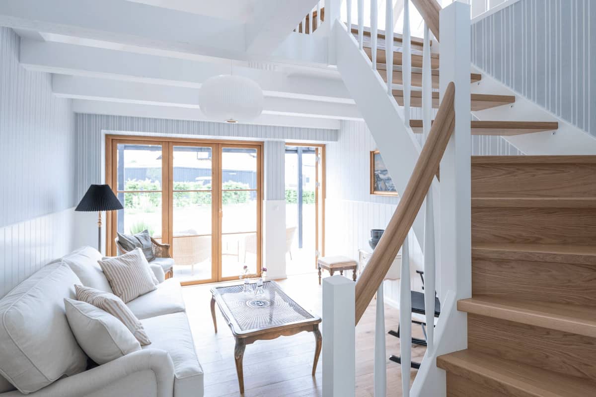A spacious living room with a white staircase, a sofa set, and a dining area.