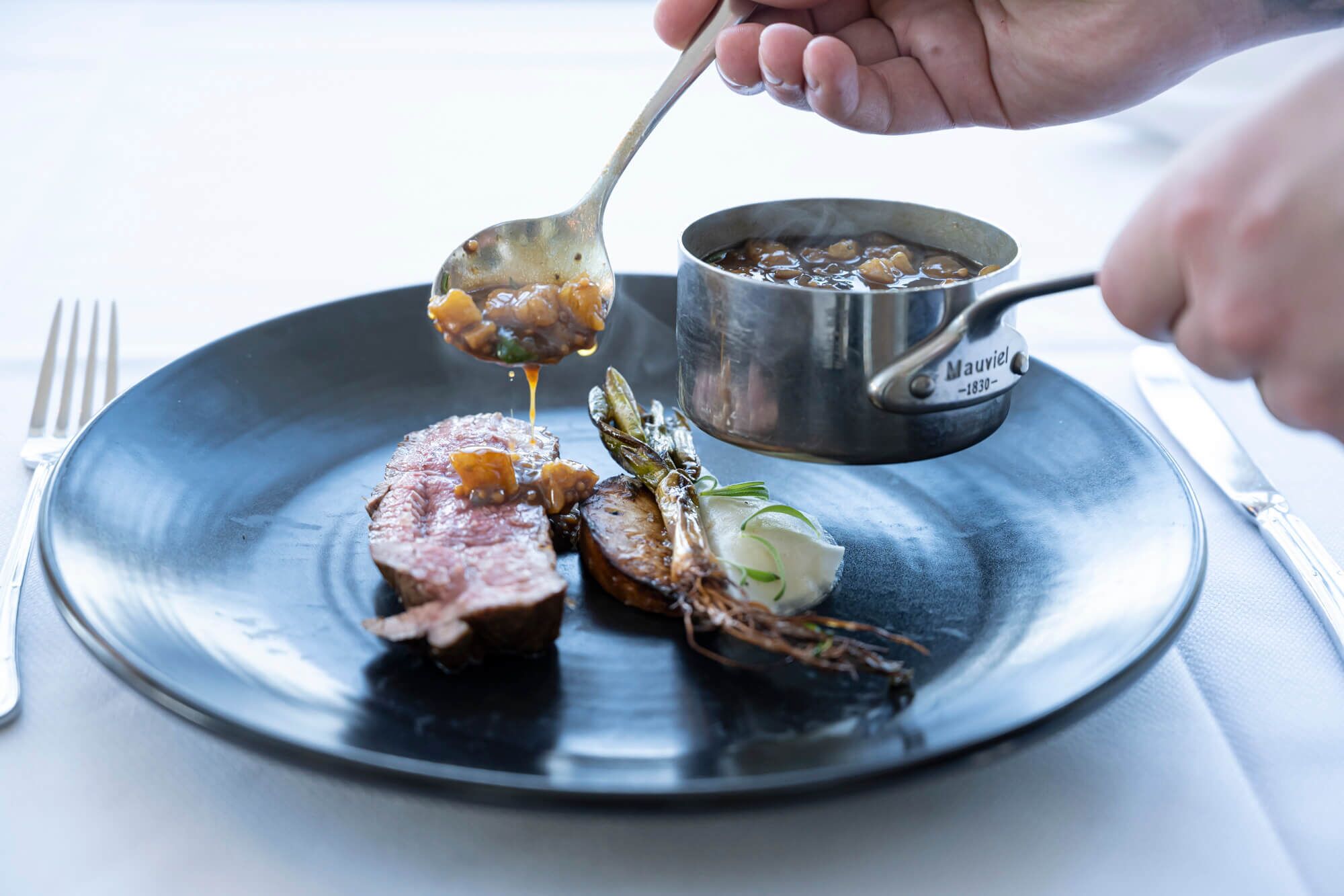 Een bord met steak en groenten, een lepel saus, en een pot ernaast.