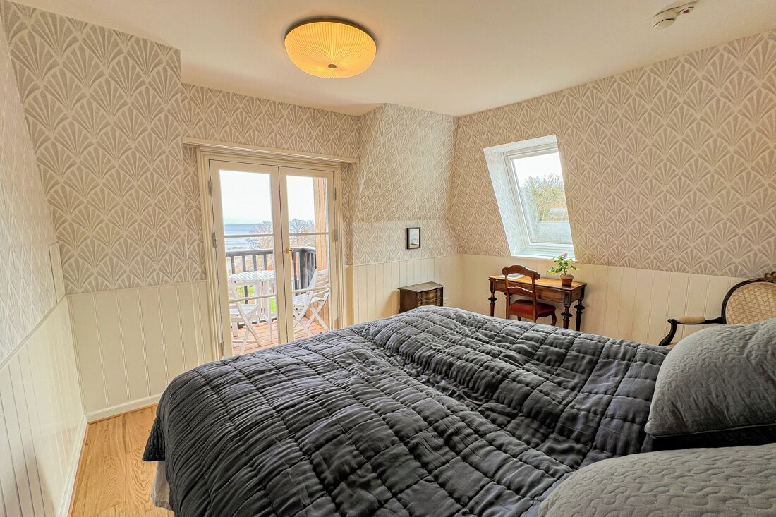 A bedroom with a large bed, a desk with a chair, a window, and a view of the outside.