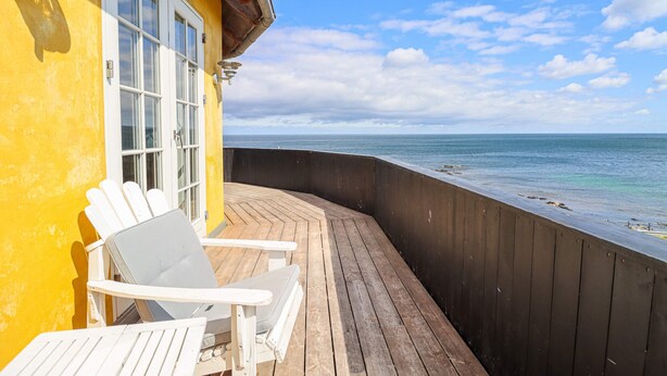 A wooden deck with a white chair and a window overlooking the ocean. - Stammershalle Badehotel & Spa (Gudhjem)
