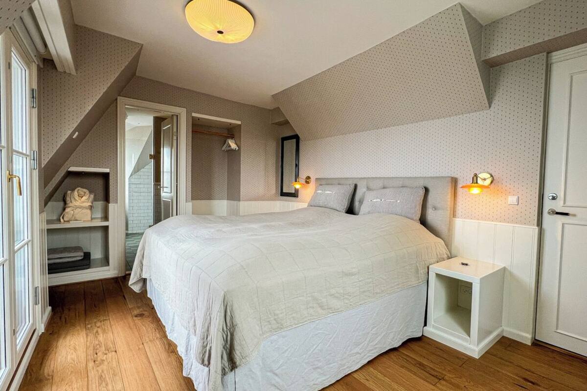 A bedroom with a large bed, a nightstand, a mirror, and a shelf with a teddy bear.