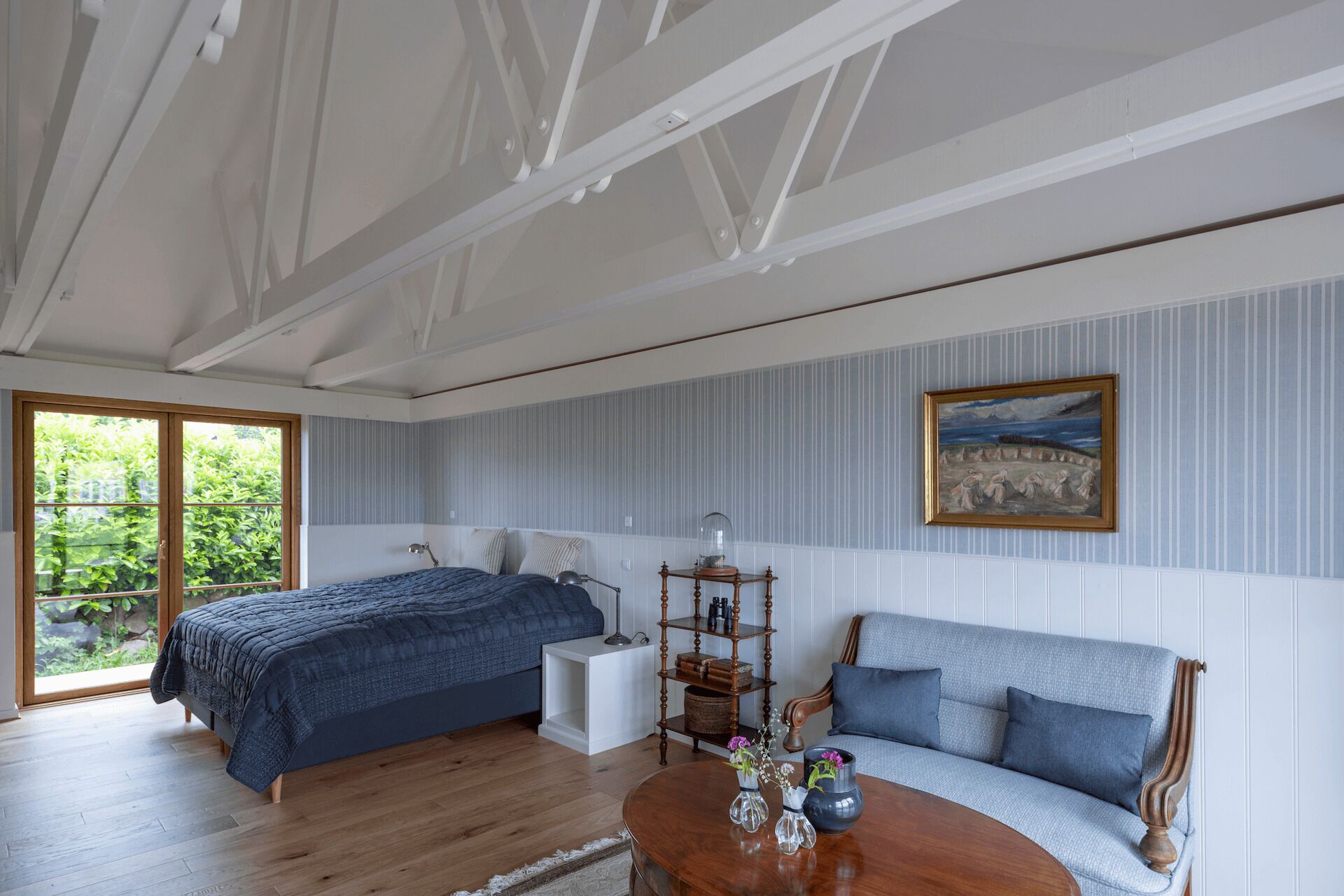 A bedroom with a bed, a sofa, a wooden coffee table, a lamp, and a painting on the wall.