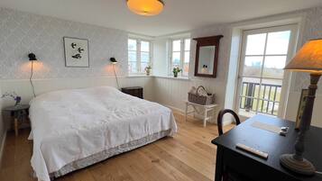 A bedroom with a large bed, two bedside lamps, a wooden desk with a lamp, a chair, and a window with a view.