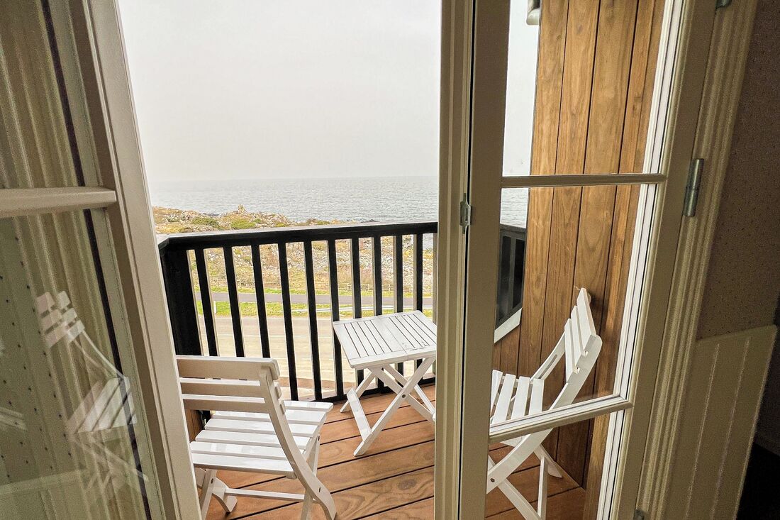 A wooden deck with white chairs and a table, overlooking a rocky coastline.