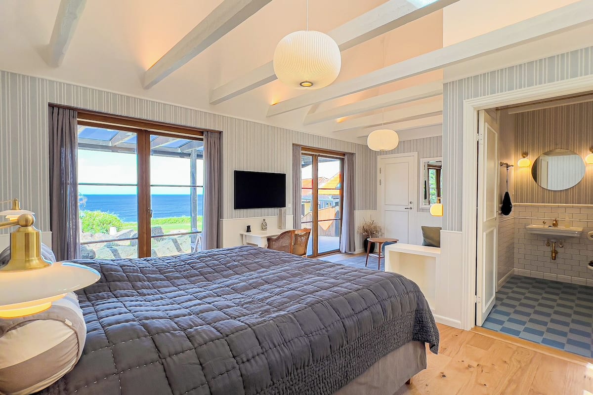 A bedroom with a large bed, a TV, and a view of the sea.