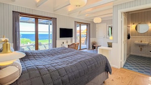 A bedroom with a large bed, a TV, and a view of the sea. - Stammershalle Badehotel & Spa (Gudhjem)