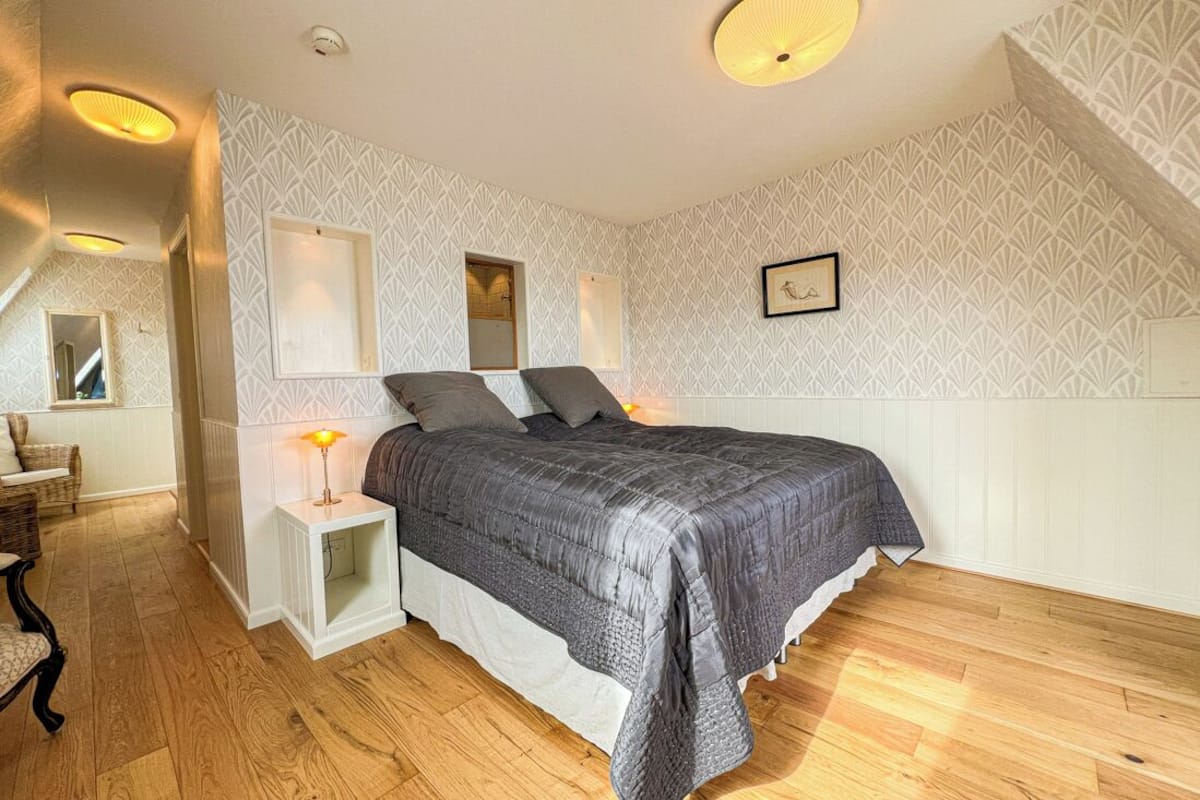 A bedroom with a bed, bedside tables, and a wall-mounted light fixture.