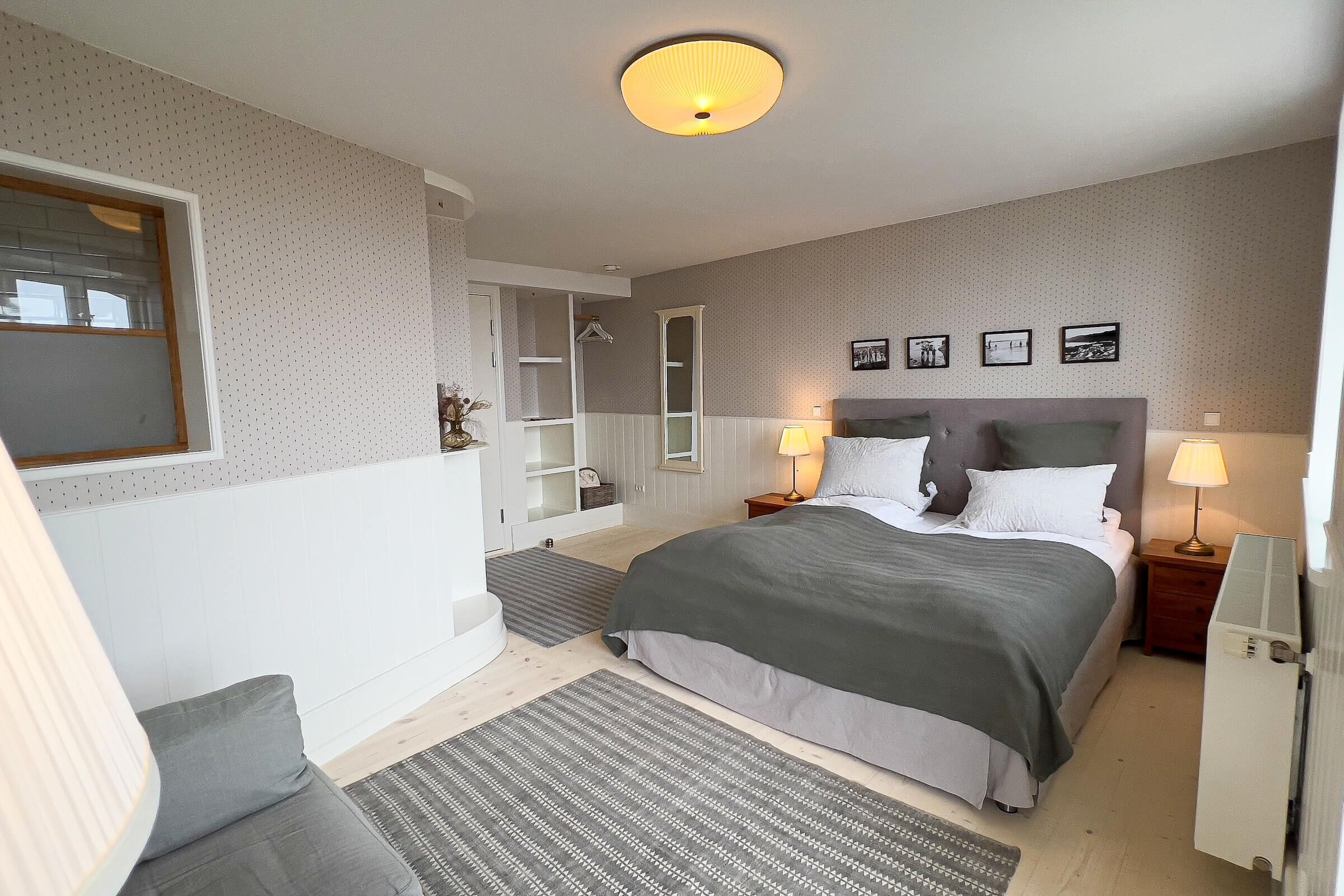 Une chambre à coucher comprenant un lit, des tables de chevet, une armoire, un miroir et une fenêtre.