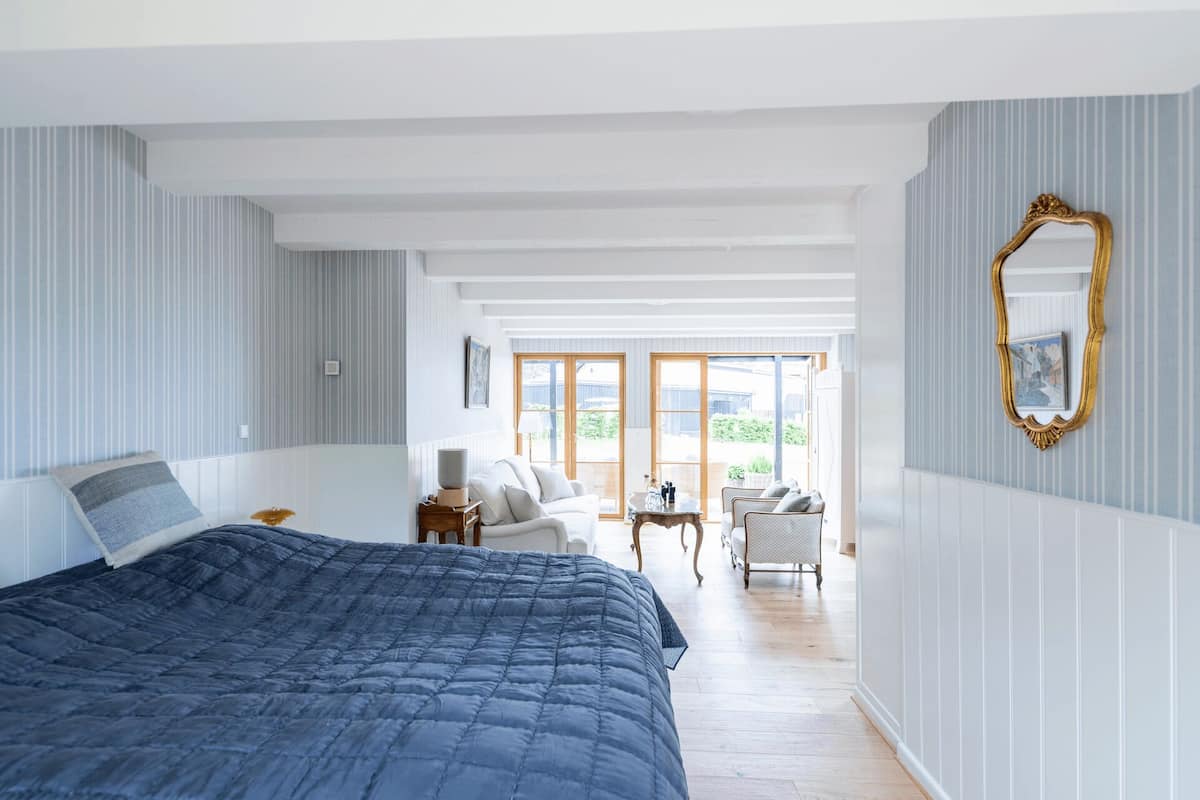 A bedroom with a large bed, a small table, a chair, and a mirror on the wall.