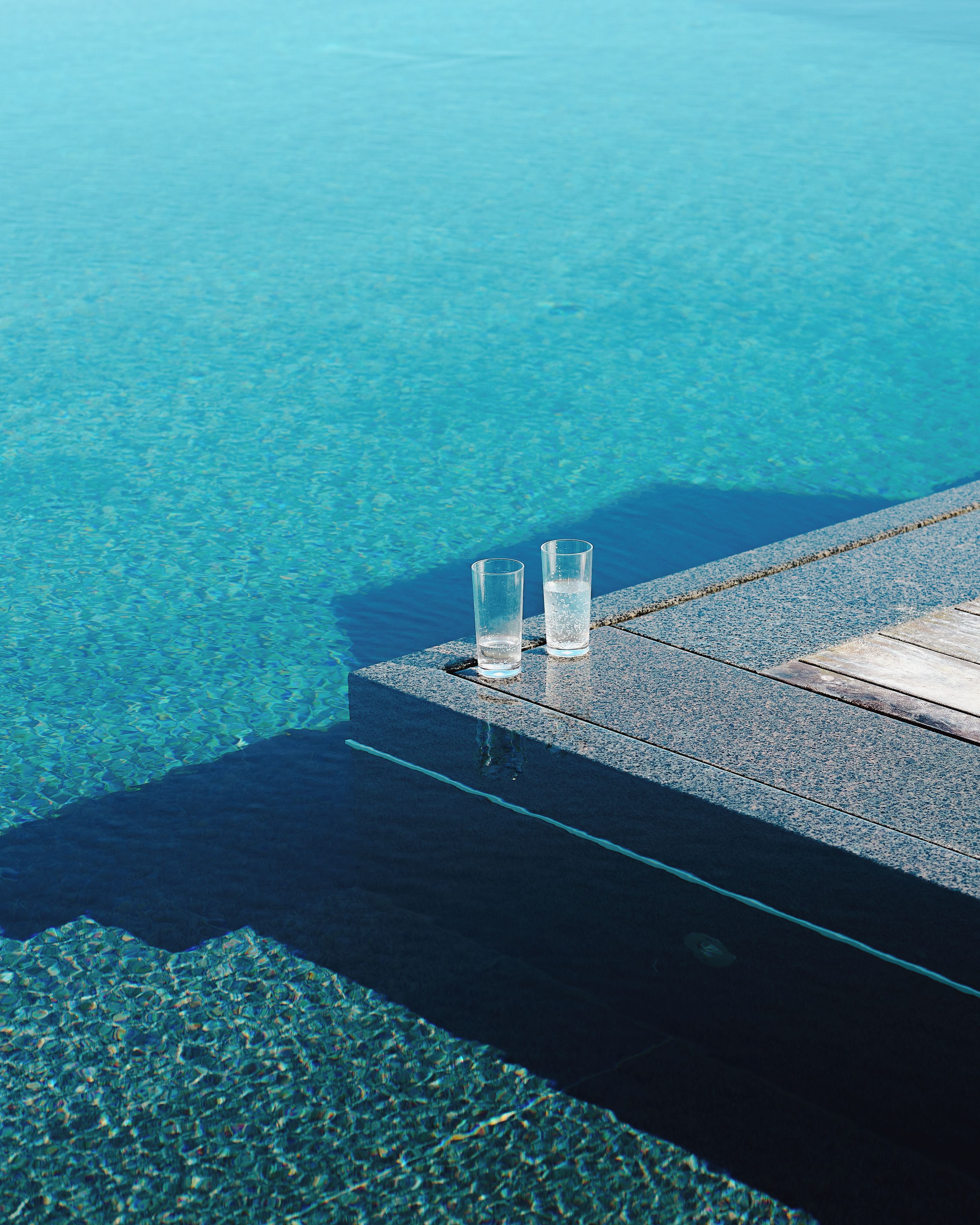 Une piscine d’eau cristalline, avec deux verres posés sur une bordure en pierre.