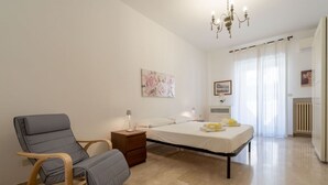 A bedroom with a bed, a chair, a nightstand, a lamp, and a painting on the wall.