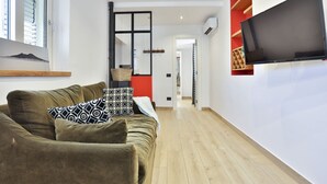 Ein Wohnzimmer mit einer Couch, einem flachbildfernseher an der Wand und Holzboden.
