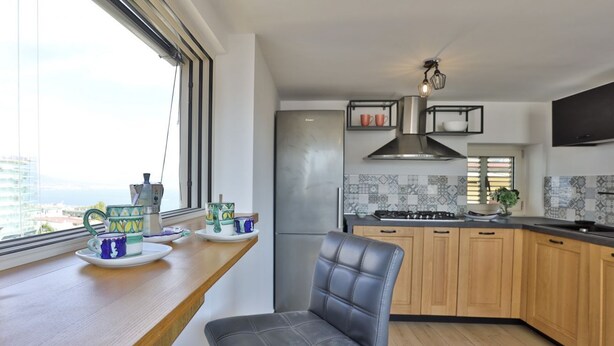 Eine moderne Küche mit eingebauter Bank, einem Edelstahl-Kühlschrank und einem Fenster mit Blick auf die Stadtlandschaft.