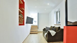 Ein modernes Wohnzimmer mit Treppe, Flachbildfernseher, Sofa und Fenster.