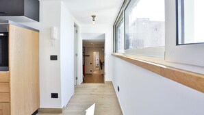 Ein schmaler Flur mit einem Holzschrank, einer Leuchte und einem Fenster mit Blick auf Gebäude.