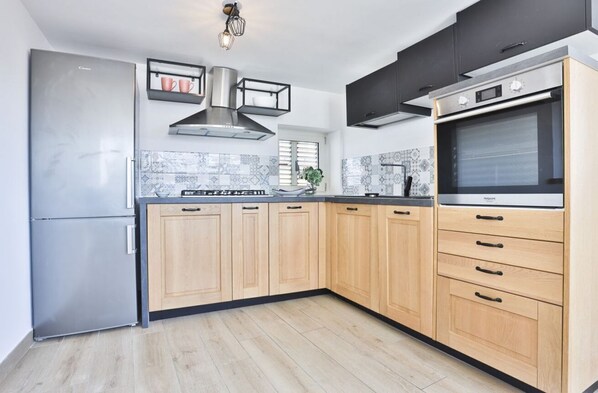 A modern kitchen with a built-in oven, stainless steel refrigerator, wooden cabinets, and a tiled backsplash.