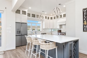 A modern kitchen with white cabinetry, a central island with bar stools, stainless steel appliances, and pendant lighting.