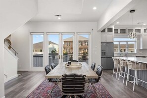 A modern kitchen with white cabinets, a central island with bar stools, and a large dining table with chairs. - Bayfront Home | Hot Tub | Private Dock | Sleeps 14 (Galveston)