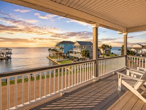 A wooden deck with a railing overlooking a body of water, with houses in the background.