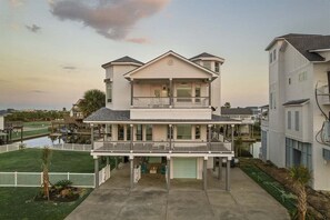 A two-story house with a balcony, a covered porch, and a garage. - Bayfront Home | Hot Tub | Private Dock | Sleeps 14 (Galveston)